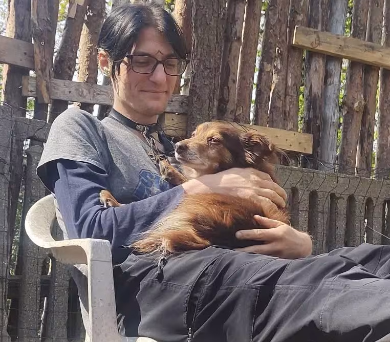 Photo of brown dog laying on person who is sitting. The person is hugging the dog.